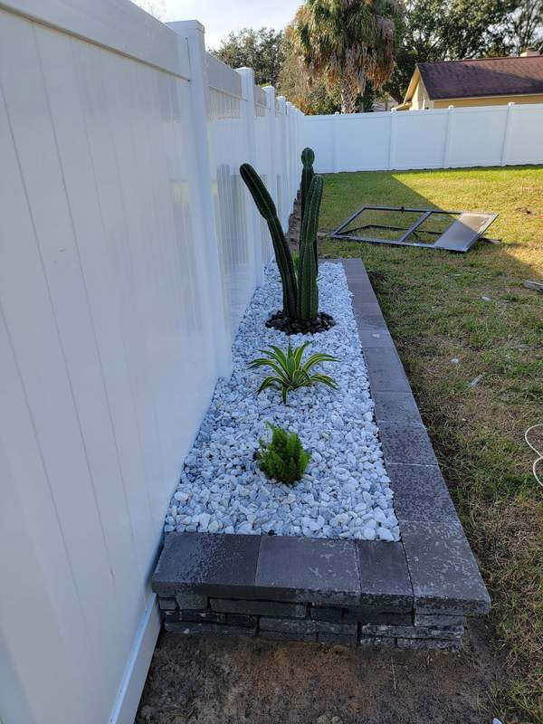 Rock garden bed with cactus and agave along a fence line
